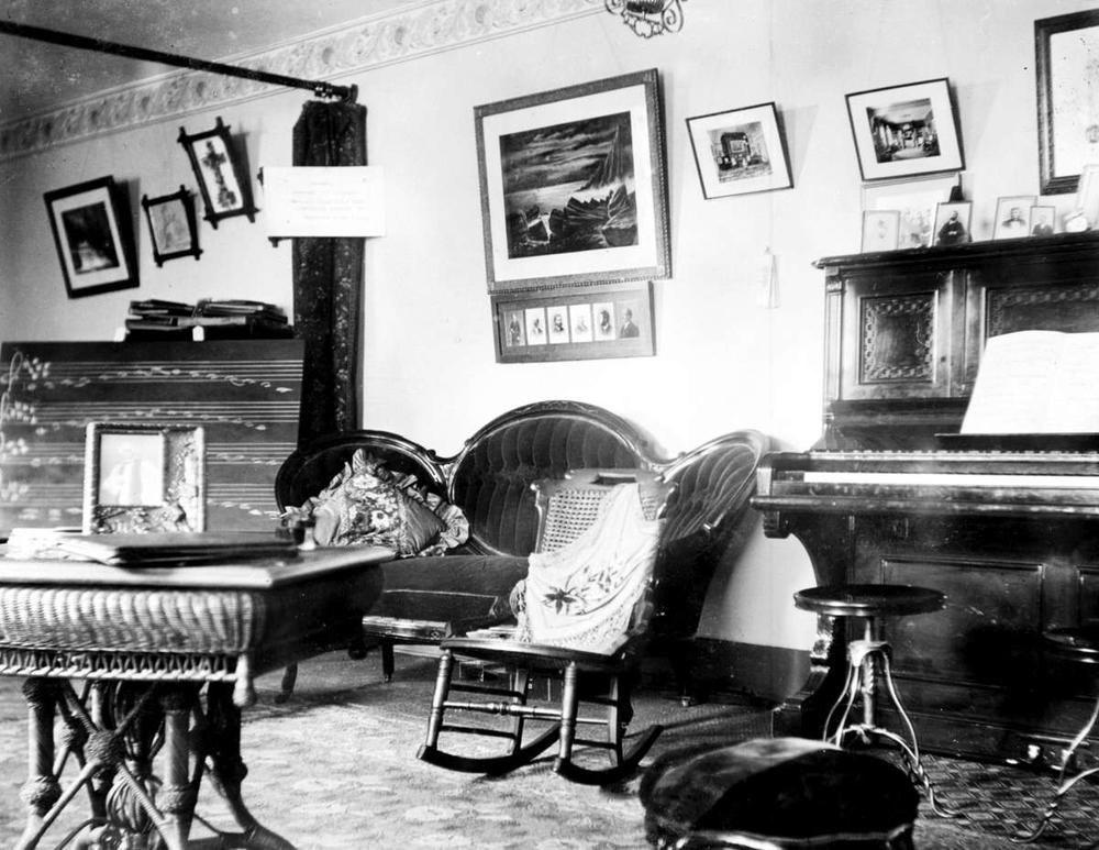 b&w music studio with piano, seating and tables, various pictures on the walls